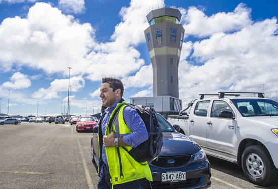 A FIFO worker in a safety jacket walks through a car park at Adelaide Airport