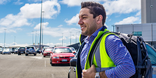 A FIFO worker in a safety jacket walks through a car park at Adelaide Airport